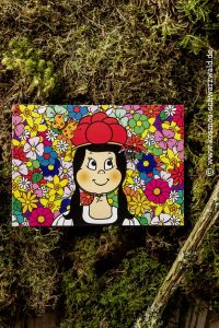 Auf dieser Postkarte ist Anni vor ganz vielen bunten Blumen zu sehen