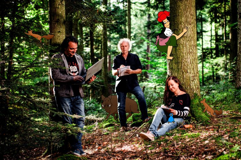 Auf dem Bild sind alle drei Autoren von Anni im Wald zu sehen und jeder arbeitet mit Laptop oder Stift und Block während Anni und die Waldtiere die drei Autoren beobachten